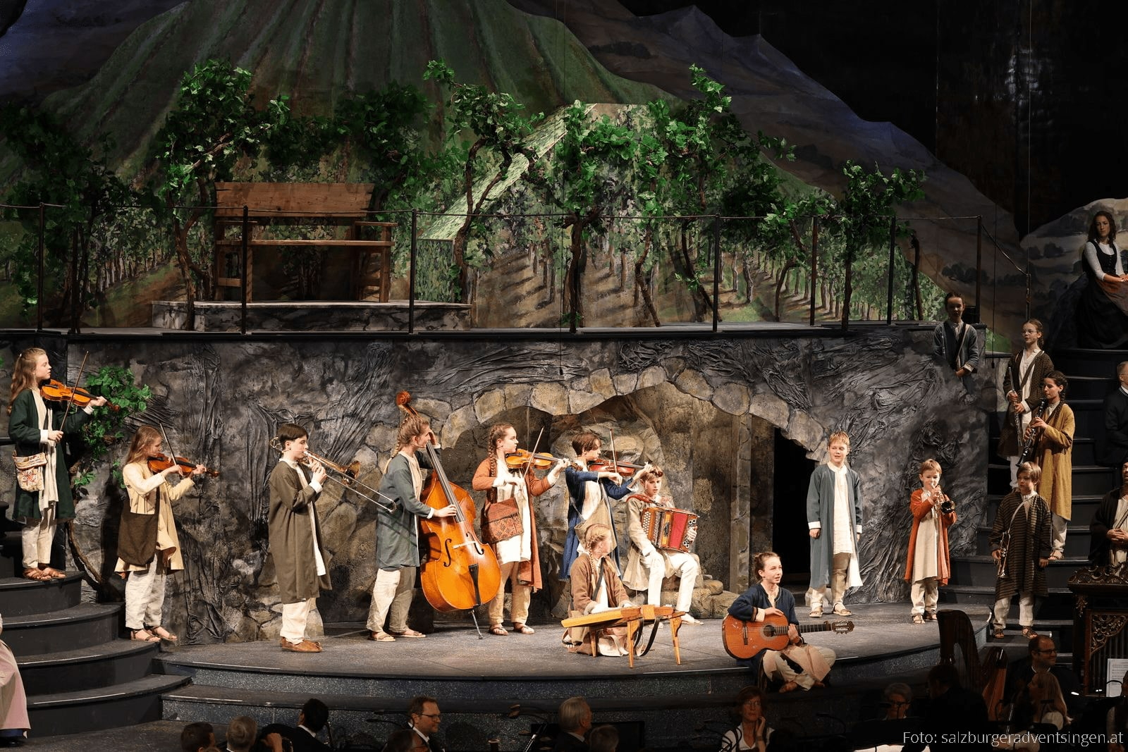 Gruppe von Darstellern mit Instrumenten vor gemaltem Bergpanorama