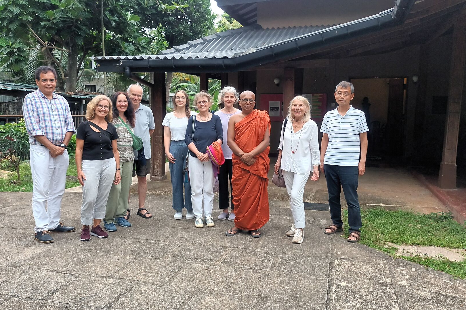 Reisegruppe steht mit Mönch in orangefarbener Robe vor Gebäude