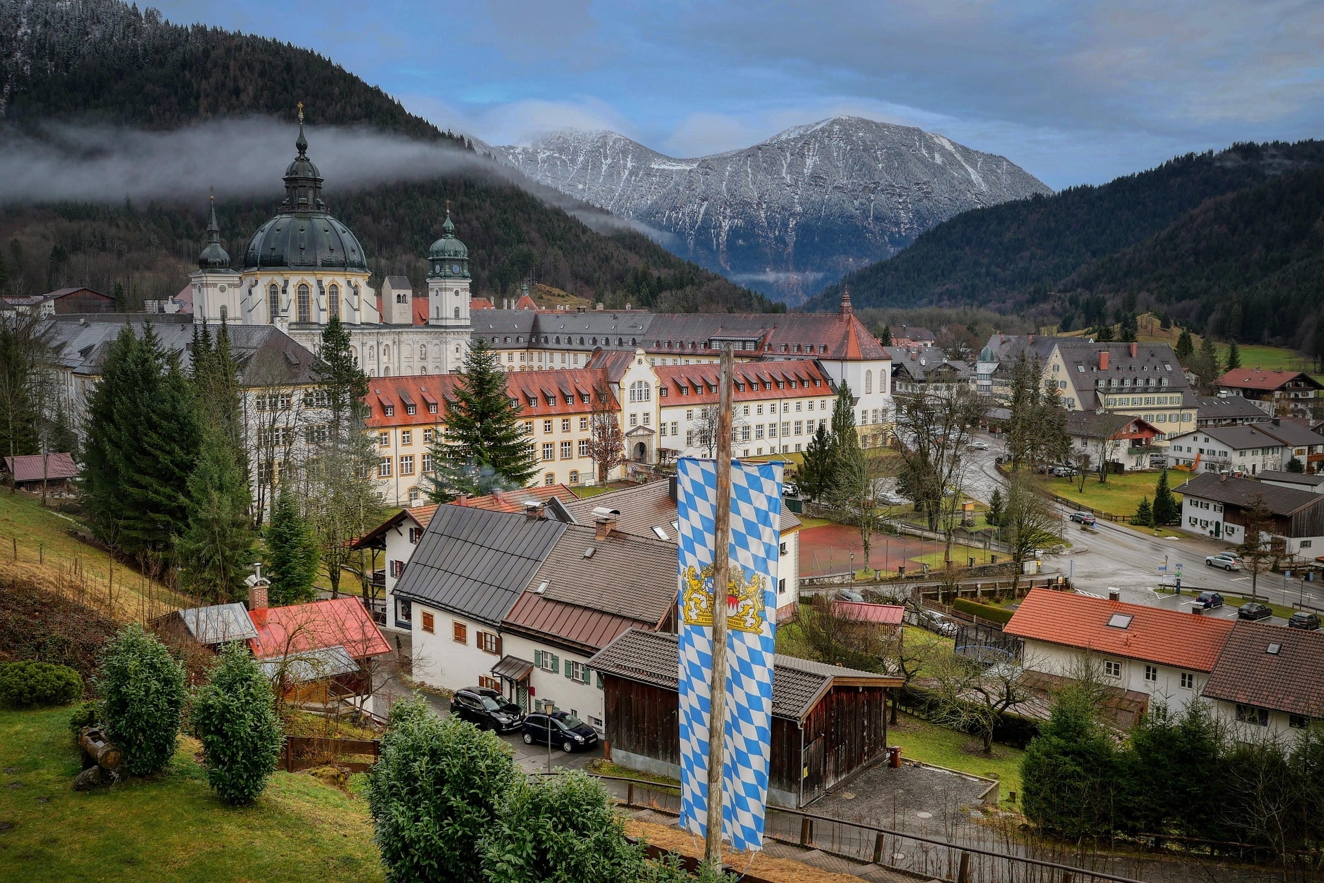 Weitläufiges Kloster mit Kuppelkirche vor Alpenkulisse