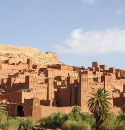 Lehmarchitektur der Kasbah Aït-Ben-Haddou am Hang mit Palmen in der Umgebung
