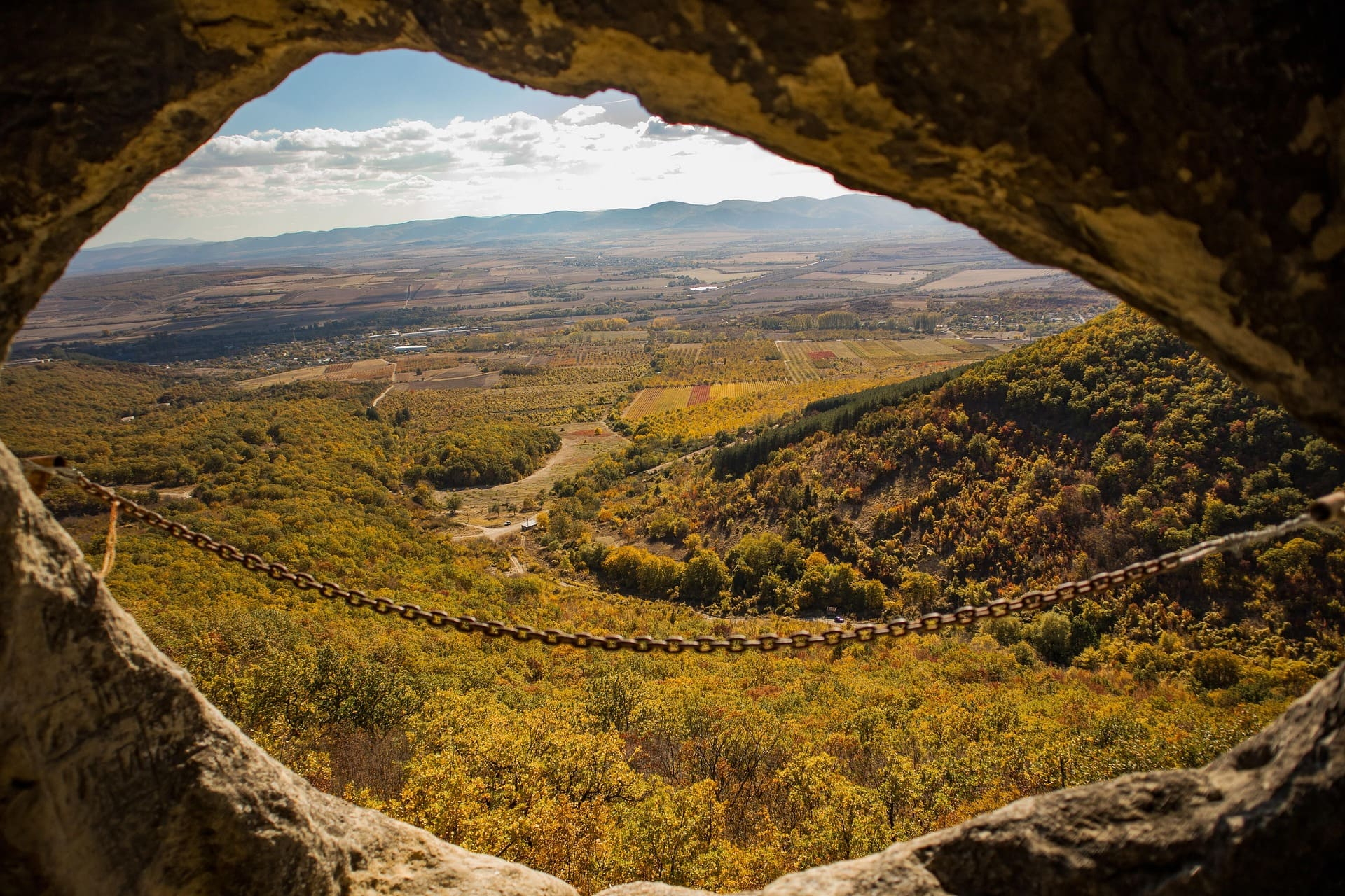 Blick durch Felsöffnung auf herbstliche Hügellandschaft und Felder