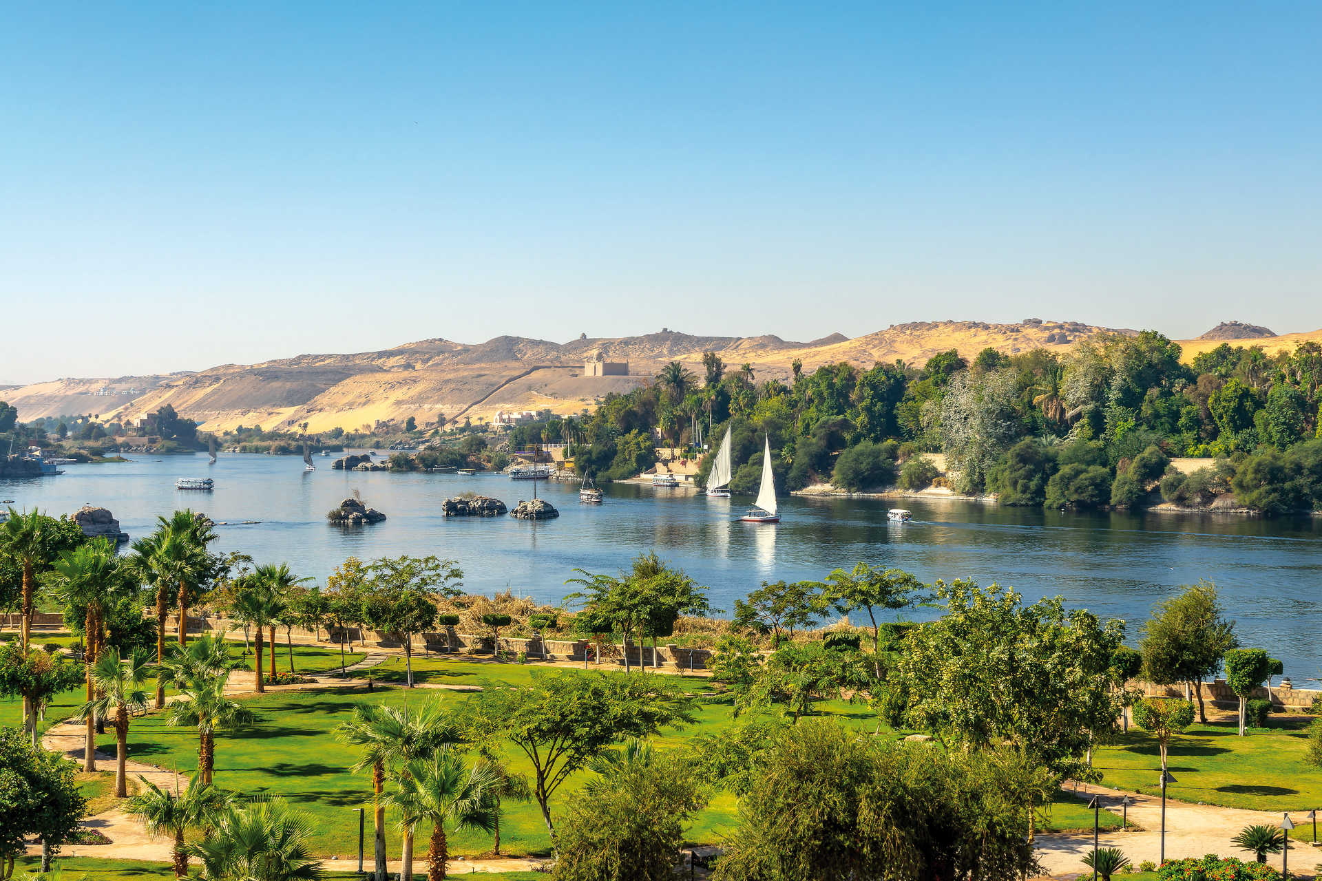 Grüne Ufer des Nils bei Assuan mit Segelbooten und Wüste im Hintergrund