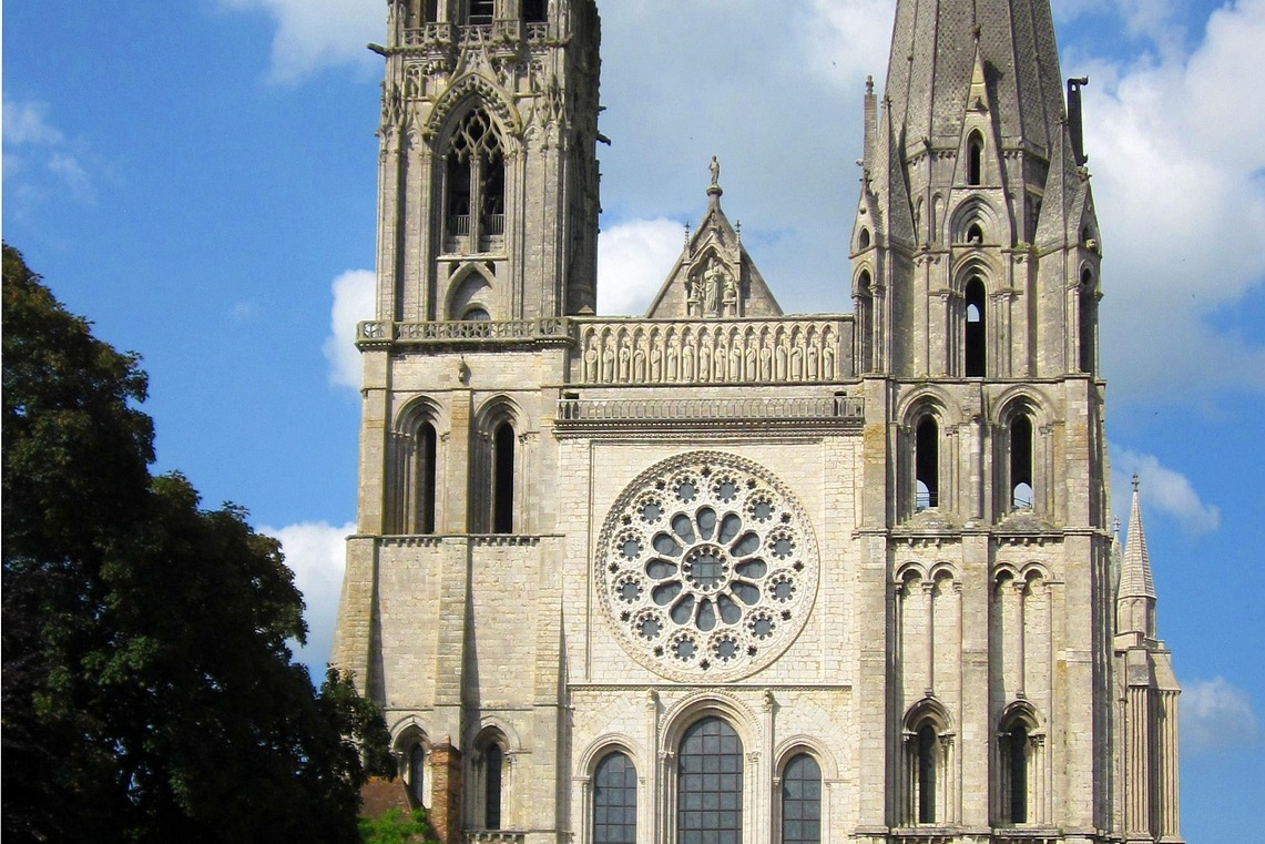 Gotische Fassade mit Rosette und zwei ungleichen Türmen unter blauem Himmel