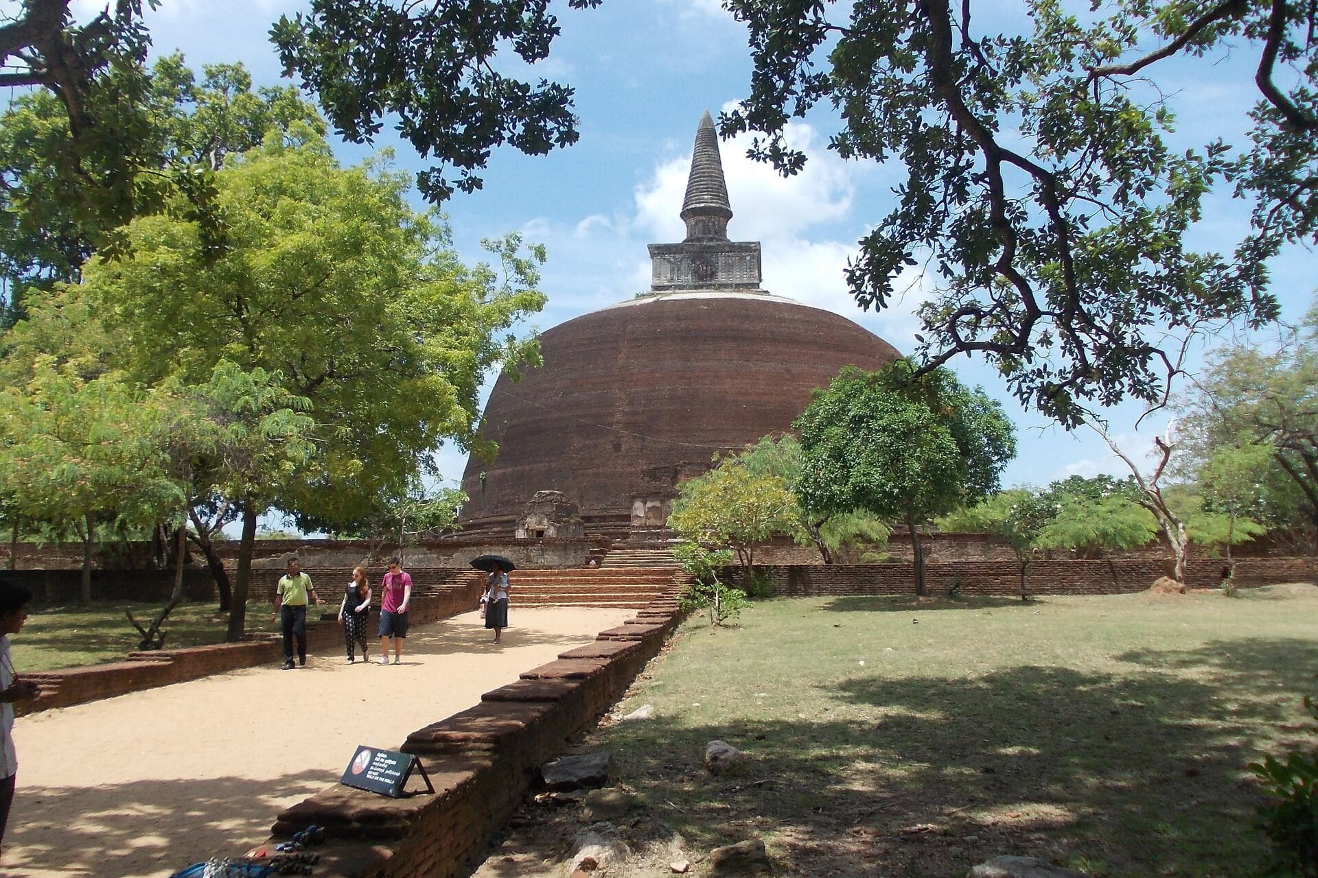 Großer roter Backstein-Stupa umgeben von Bäumen und Besuchern