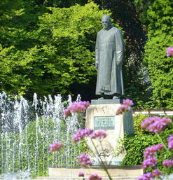 Statue von Sebastian Kneipp vor Springbrunnen und grünen Bäumen