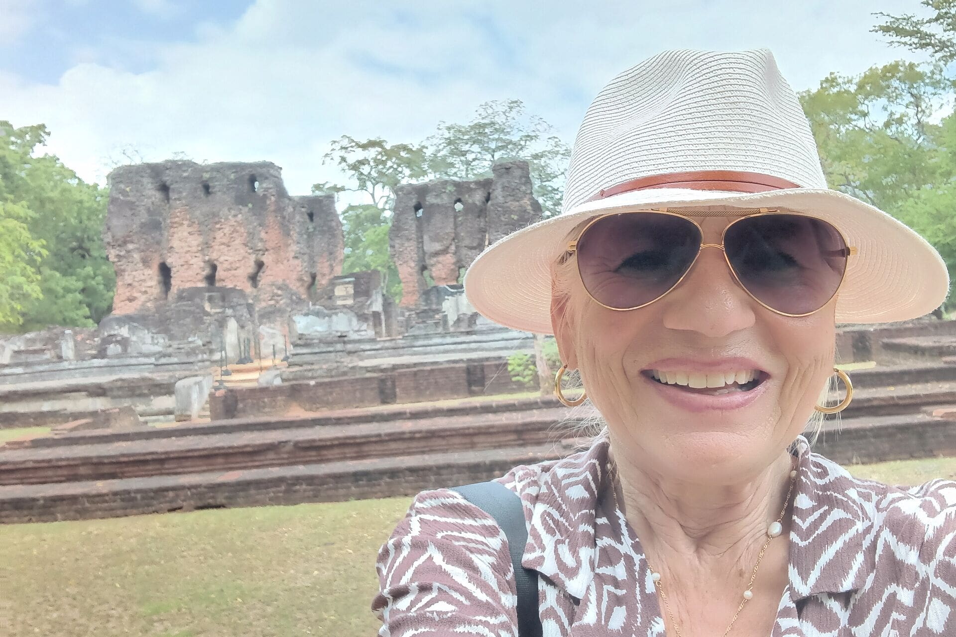 Frau mit Sonnenhut lächelt vor alten Backsteinruinen im Grünen