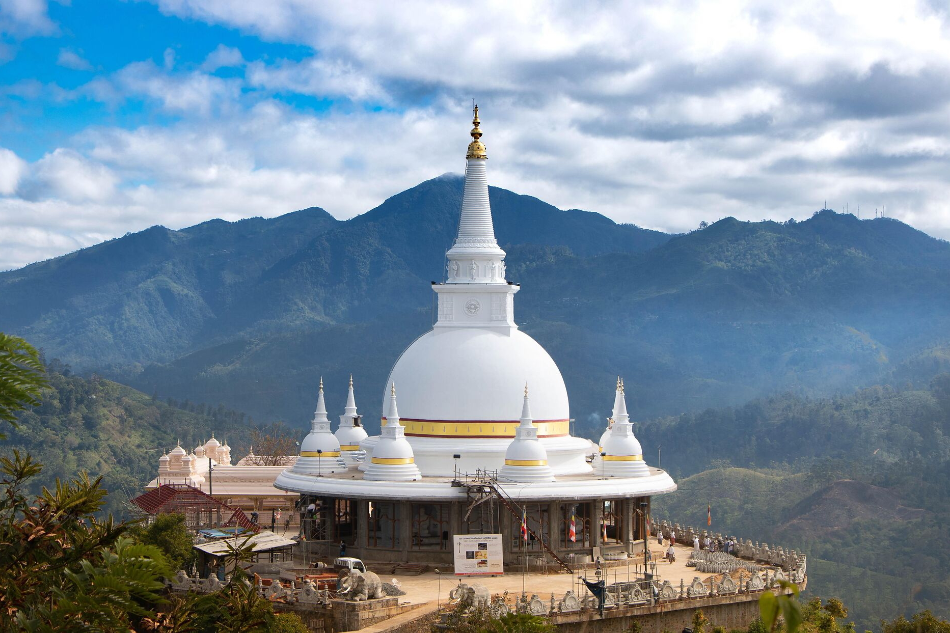 Buddhistischer Stupa mit goldenen Details vor grüner Berglandschaft