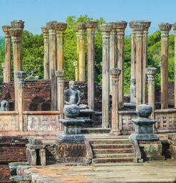 Ruinen eines historischen Tempels mit aufrecht stehenden Steinsäulen, sitzenden Buddha-Statuen und umgeben von dichter tropischer Vegetation