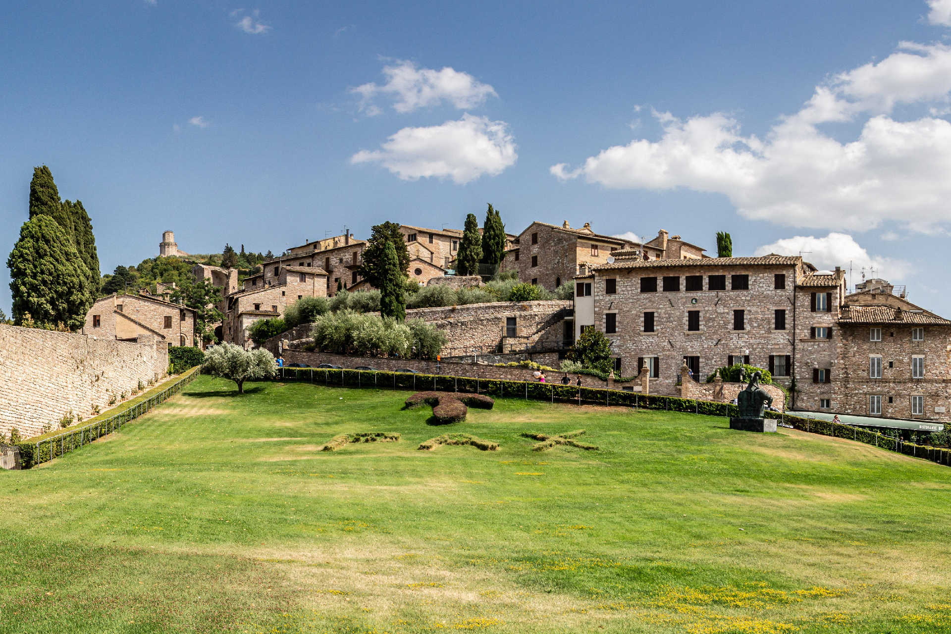 Historische Steinhäuser auf einem Hügel mit Gärten und Zypressen unter blauem Himmel