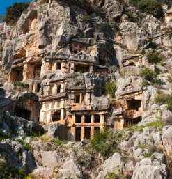 Antike Grabfassaden in steiler Felswand umgeben von Büschen und Bäumen