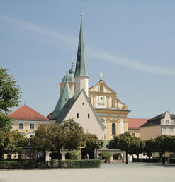Stadtplatz mit Bäumen und Kirche mit spitzem Turm