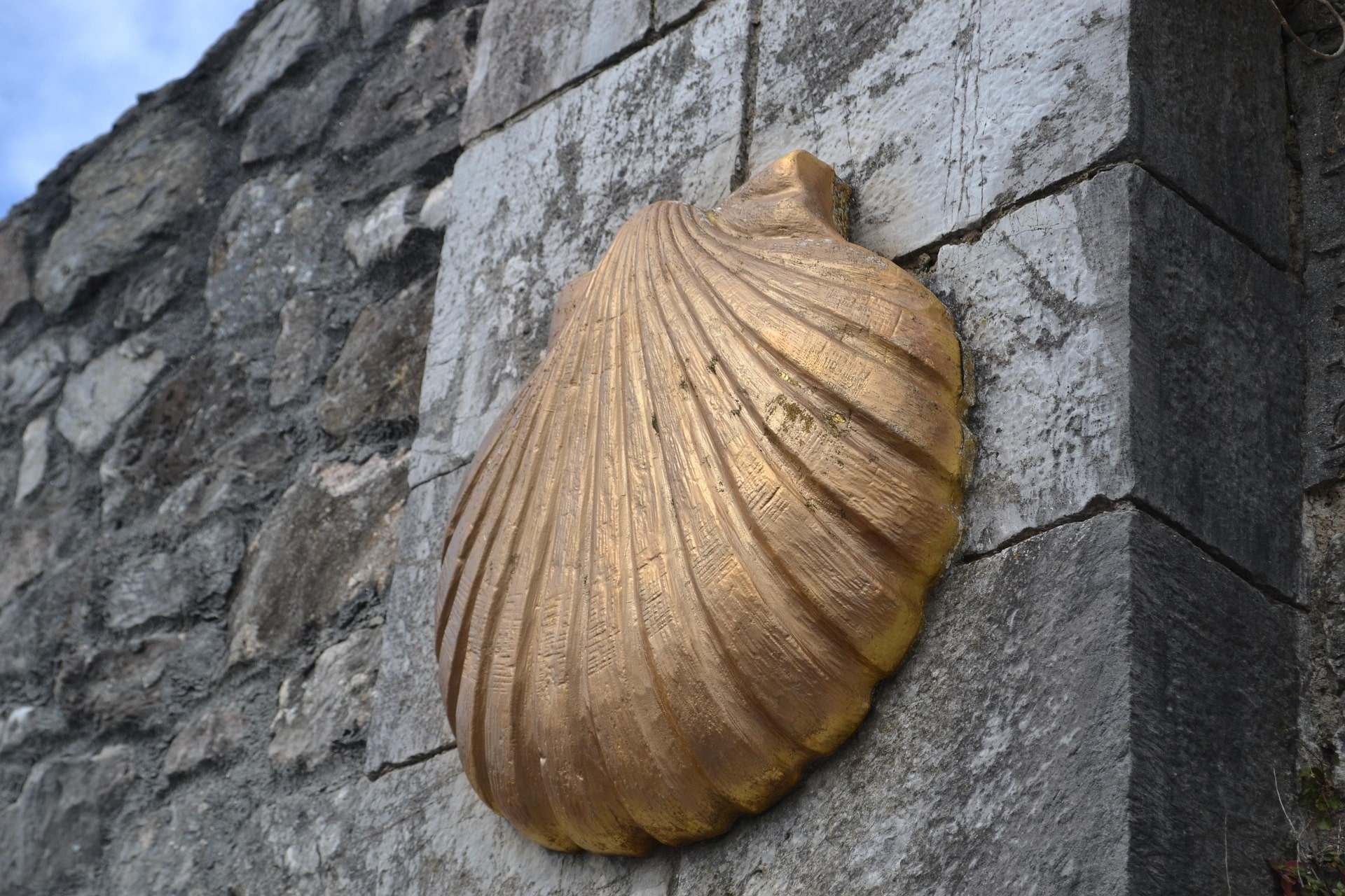 Große goldene Muschel als Pilgerzeichen an Steinmauer