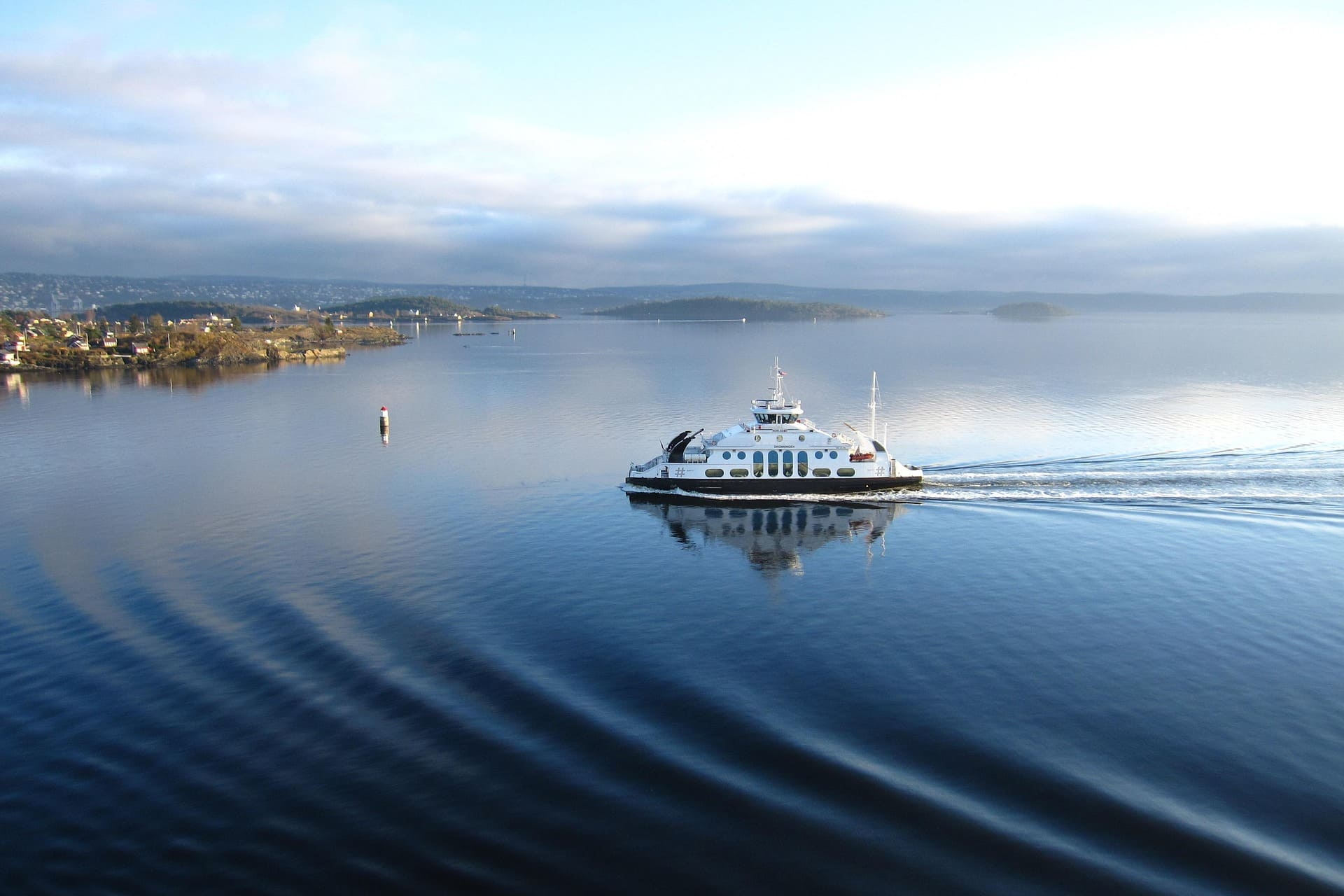 Weiße Fähre zieht Wellen über ruhigen Fjord bei Morgenlicht