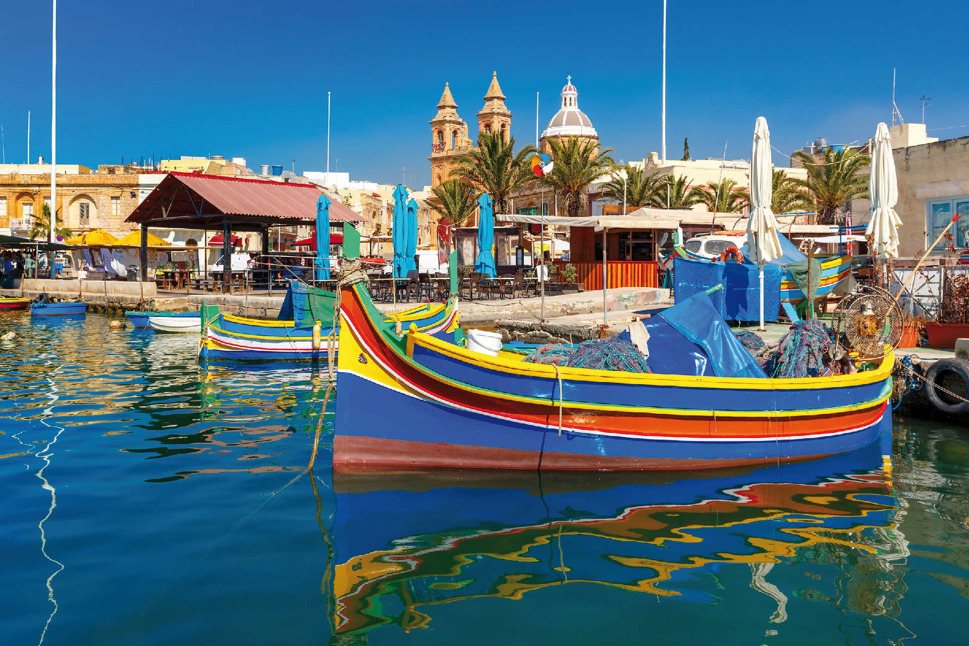 Bunte Fischerboote im Hafen von Marsaxlokk mit Kirche und Marktständen