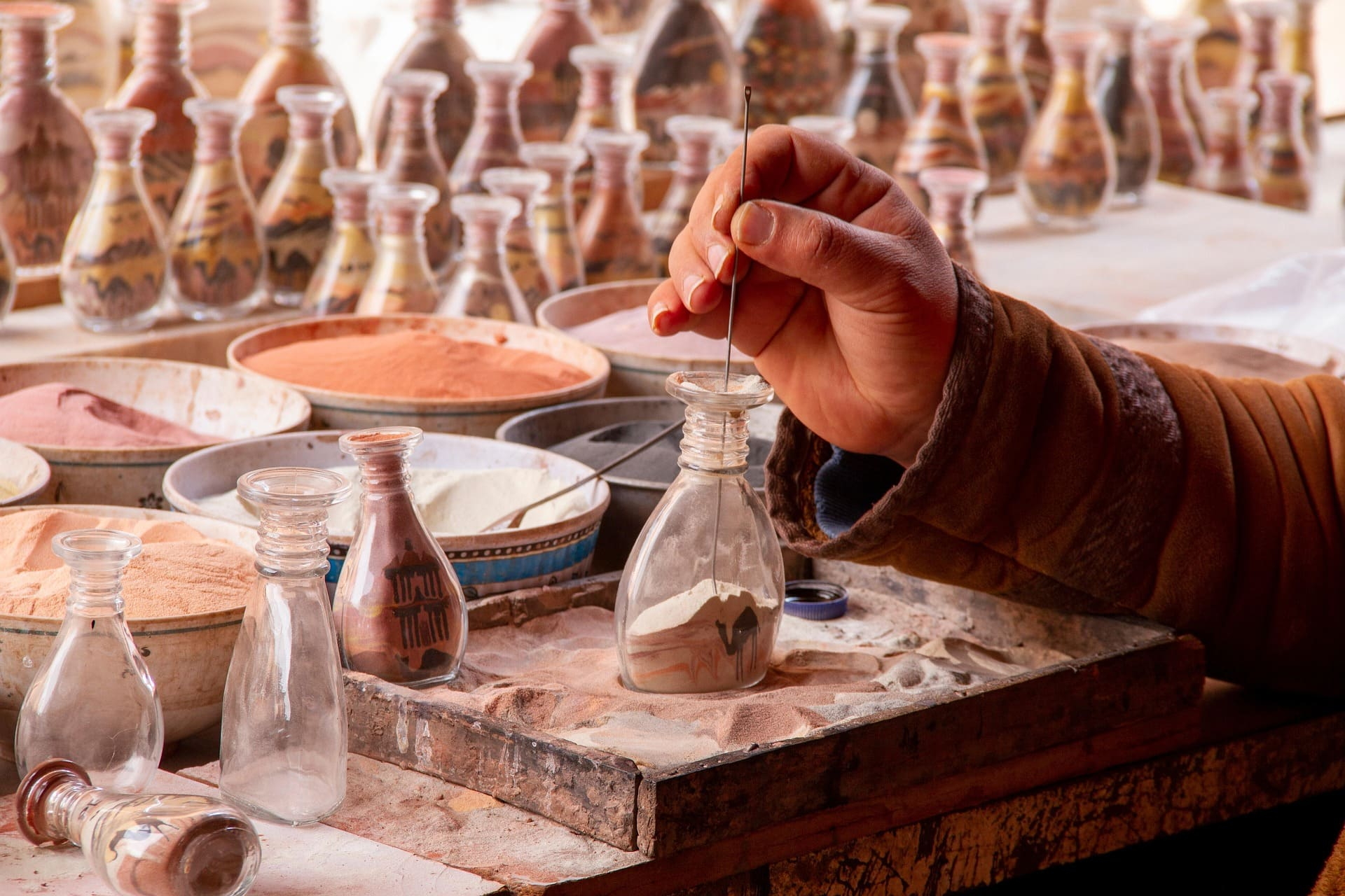 Hand füllt bunt geschichteten Sand in Glasflaschen mit Mustern