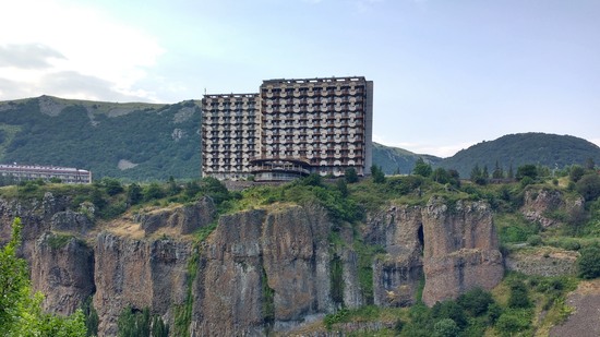 Großer Betonbau erhebt sich auf steilem Felsen über grünem Tal