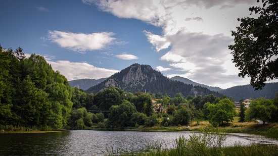 Ruhiger See von Bäumen umgeben mit Bergmassiv im Hintergrund