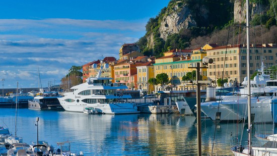 Weiße Yachten liegen vor bunten Häusern am Hafen unter Felsen
