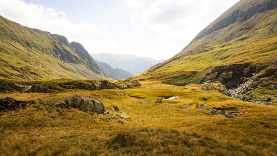 Grasbewachsenes Hochtal mit Felsen zwischen sanften Bergflanken