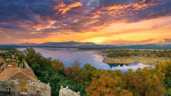 Sonnenuntergang färbt Himmel über See mit Wäldern und Bergen