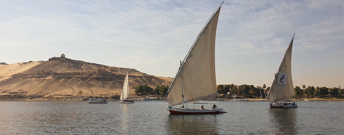 Segelboote auf dem Nil bei Assuan vor Wüstenhügel mit Ruinen im Abendlicht