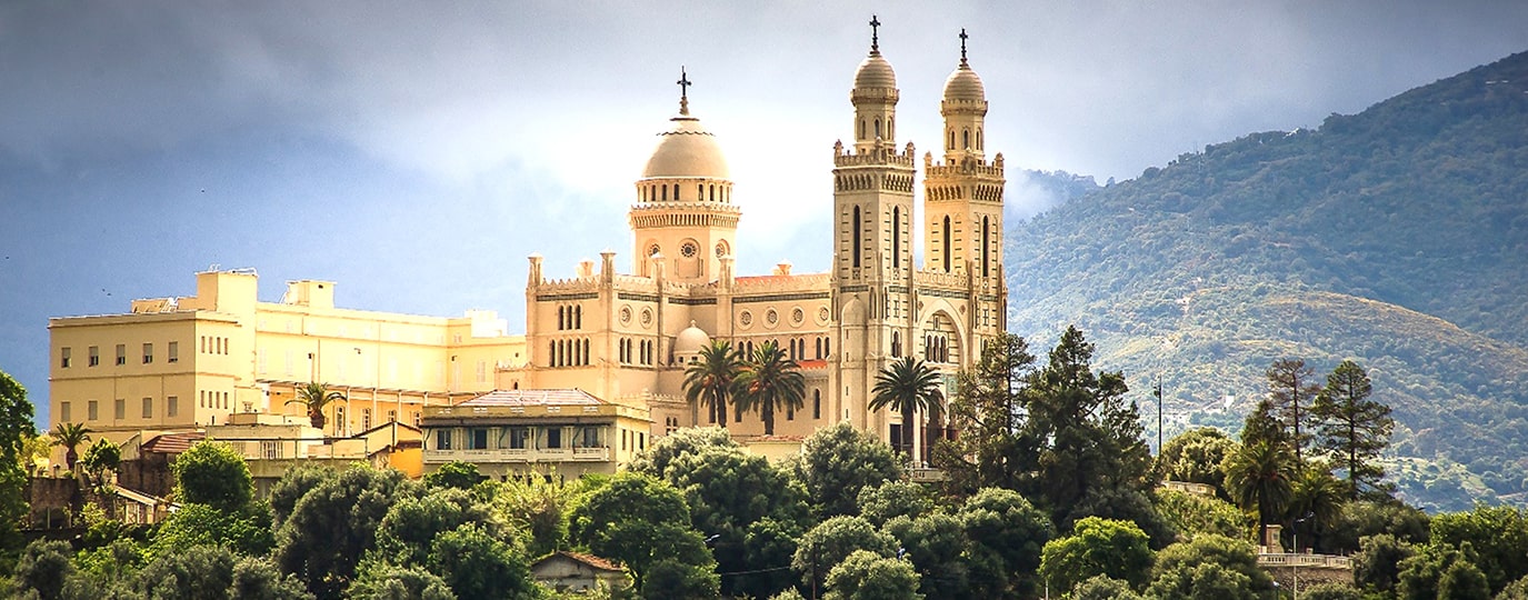 Große weiße Basilika mit Kuppeln und Türmen auf grünem Hügel