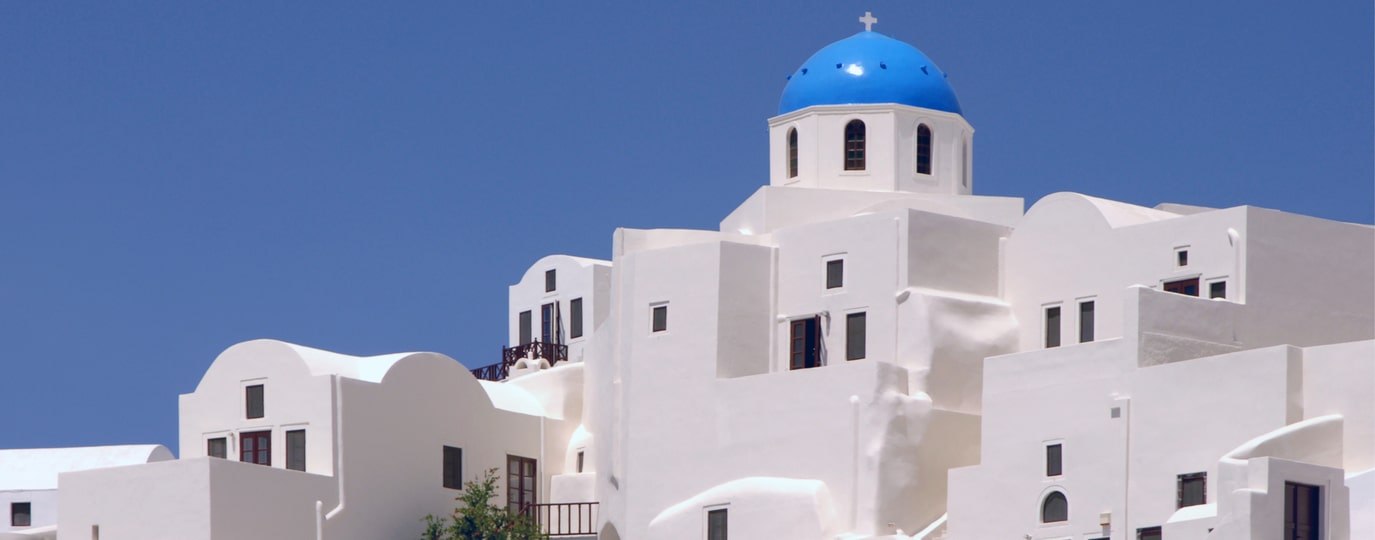 Weiße Häuser mit blauer Kuppelkirche auf Santorin vor wolkenlosem Himmel