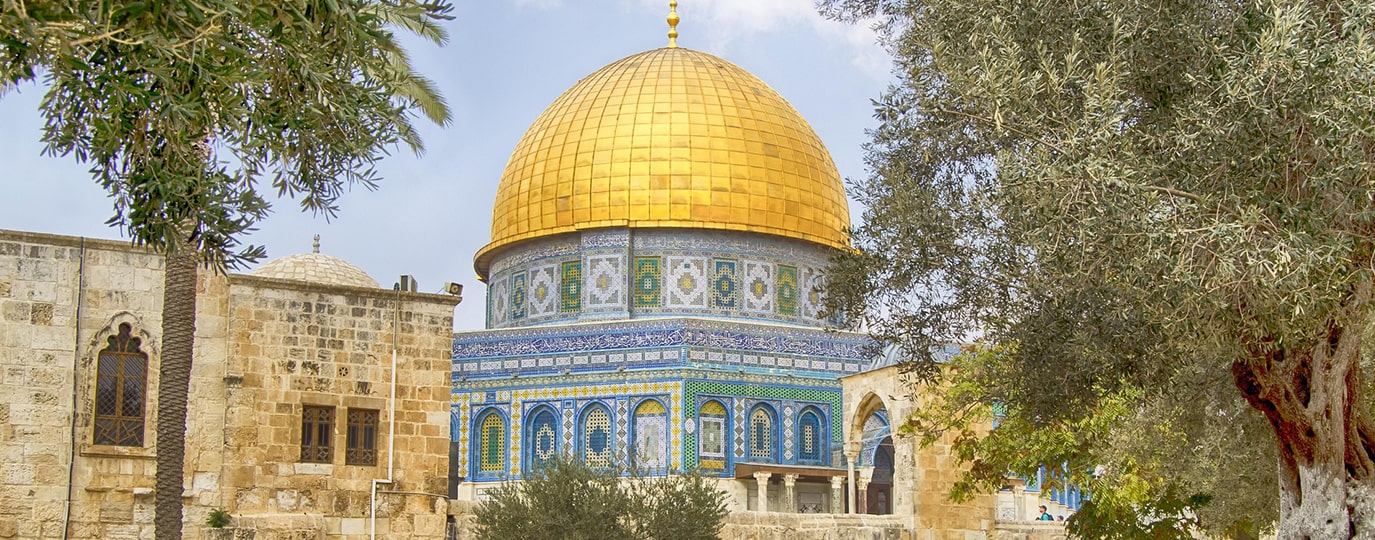 Vergoldete Kuppel und blau verzierte Fassade des Felsendoms zwischen Bäumen