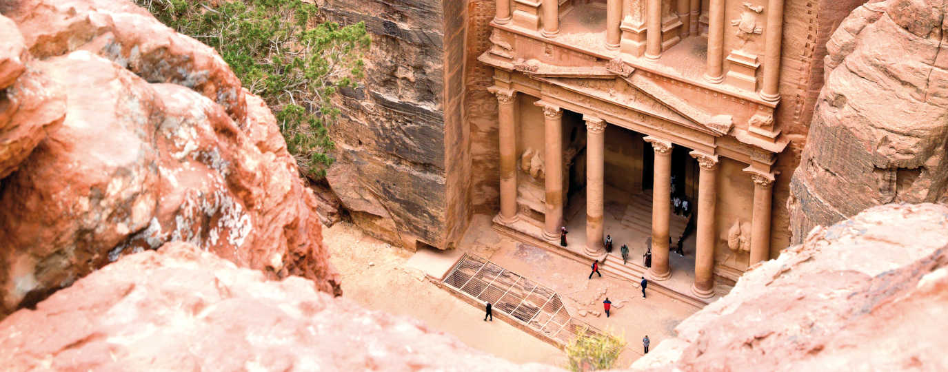 Antike Tempelfassade in rosafarbenem Fels mit Besuchern in der Schlucht von Petra