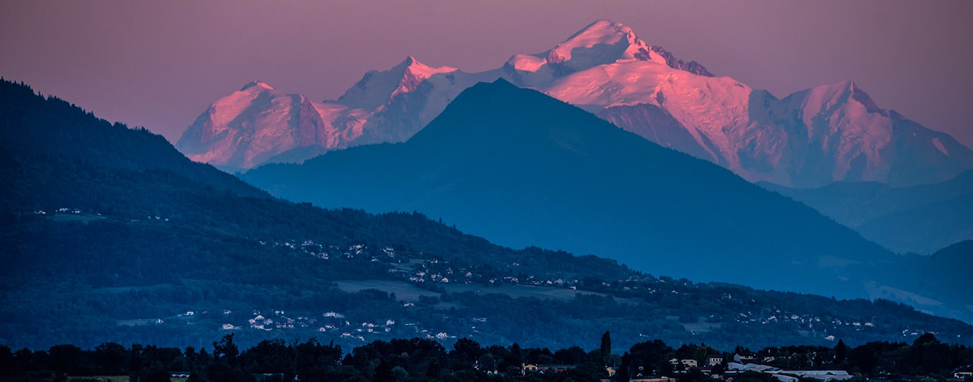 Schneebedeckter Mont Blanc im Abendlicht über dunklen Hügeln