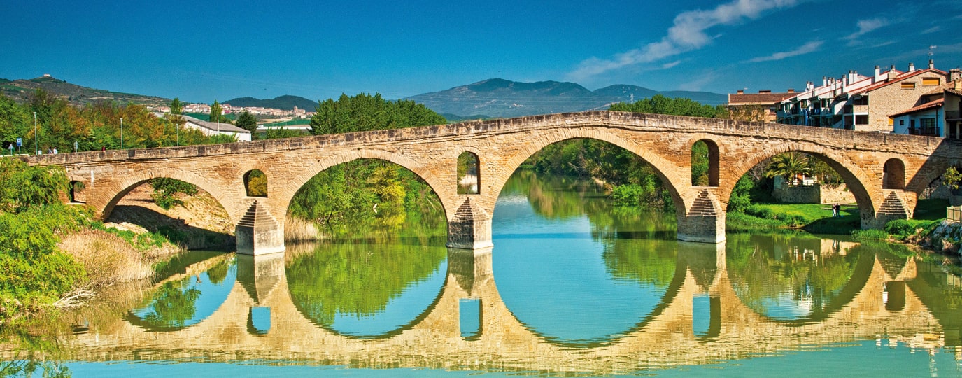 Historische Steinbrücke mit Rundbögen spiegelt sich im ruhigen Fluss