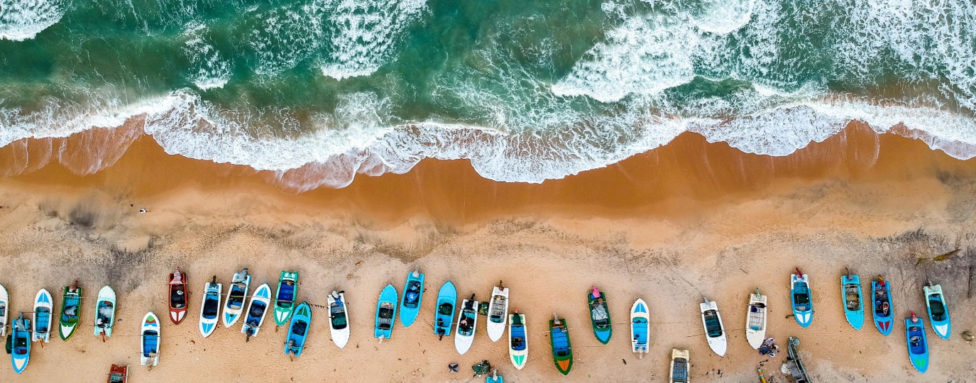 Farbige Fischerboote auf Sandstrand, Wellen brechen an der Küste