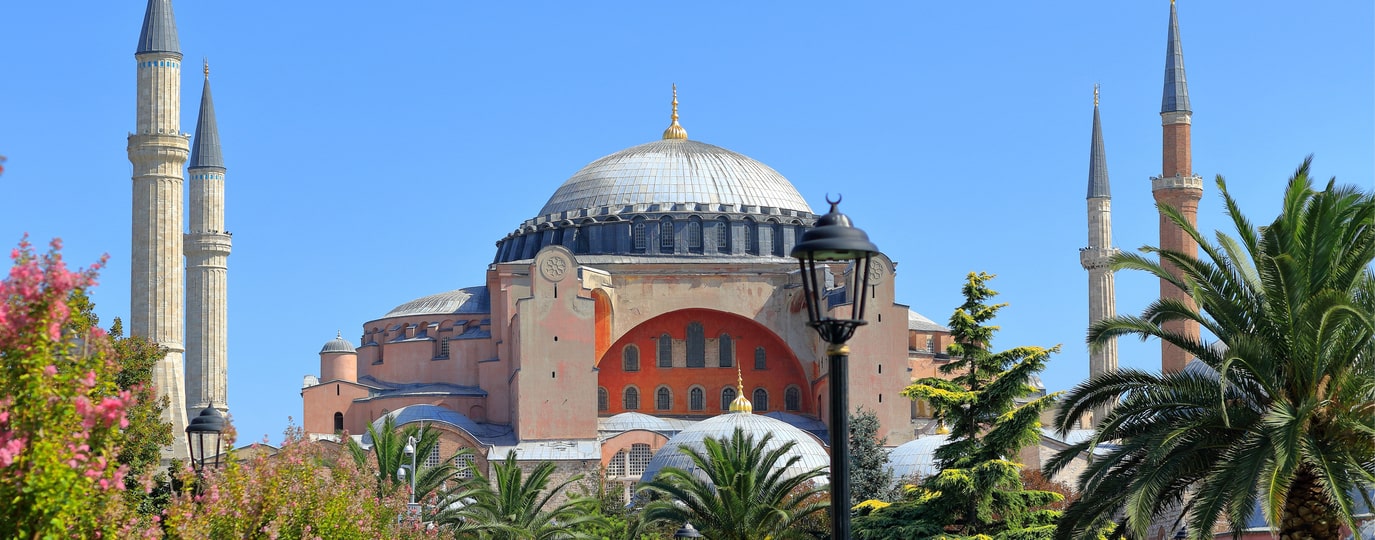 Blick auf die Hagia Sophia mit vier Minaretten und Palmen unter blauem Himmel
